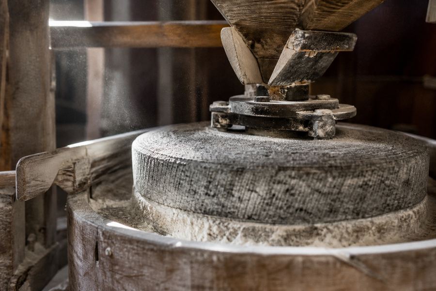 A pair of granite millstones under a wooden hopper, the surfaces dusted white with flour.