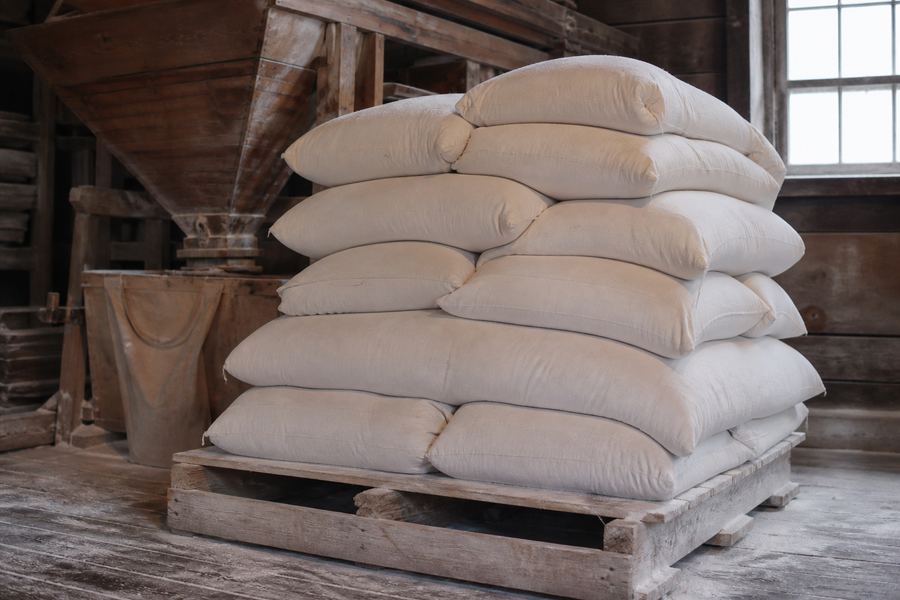 Filled cloth flour sacks stacked on a wooden pallet beneath the mill's hoppers.